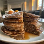 Delicious gingerbread pancakes on a plate, featuring vibrant orange slices and a creamy topping.