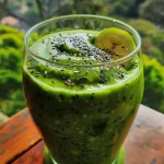 A thick avocado smoothie in a clear glass, with a straw positioned for drinking.