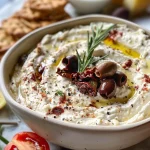 Juicy whipped feta dip in a white bowl, surrounded by crackers and fresh vegetables.