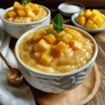 Textured mango pudding highlighted with mango pieces and mint for a refreshing touch.