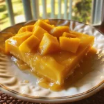 Juicy mango pudding served in a bowl, garnished with diced mango and a spoon beside it.