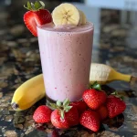 A nutritious protein smoothie featuring fresh strawberries and a slice of banana, served in a clear glass.