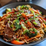 A close-up view of a colorful beef stir-fry with noodles and vegetables.