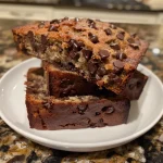 Close-up of a slice of moist chocolate chip banana bread with chocolate chips and a buttered crust.