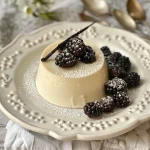A dessert consisting of Vanilla Bean Panna Cotta with a rich berry compote, captured in a close-up side view.