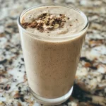Close-up of a creamy vanilla protein smoothie in a glass, garnished with a slice of banana.