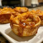 ['Juicy BBQ Chicken Cups in a silver baking tray, side view showing flaky crescent dough and melted cheese.', 'Close-up of BBQ Chicken Cups, highlighting golden brown crescent dough and rich barbecue sauce.', 'Flaky BBQ Chicken Cups with visible chicken and cheese filling, taken from the side.', 'A close-up view of BBQ Chicken Cups, golden and bubbly, with a tantalizing barbecue topping.']