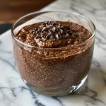 ['A close-up side view of a creamy chocolate chia pudding in a glass.', 'A rich chocolate chia pudding topped with a sprinkle of cocoa powder.', 'A side view of delicious chocolate chia pudding with a smooth texture.', 'A close-up of chocolate chia pudding featuring layers of creamy texture.']