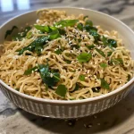 ['A close-up side view of a bowl of Easy Garlic Butter Ramen topped with a fried egg.', 'Juicy Easy Garlic Butter Ramen in a bowl, featuring leafy greens and garlic.', 'A vibrant bowl of ramen with butter, garlic, and greens, garnished with fresh basil.', 'Close-up of delicious garlic butter ramen noodles with sesame seeds and black pepper.']