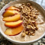 ['A vibrant Peach Smoothie Bowl topped with colorful fruits and granola.', 'Close-up of a creamy Peach Smoothie Bowl garnished with nuts and coconut.', 'A side view of a smoothie bowl filled with peach yogurt and frozen peaches.', 'Textured Peach Smoothie Bowl featuring banana and various toppings.']
