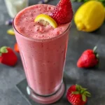 ['Close-up view of a vibrant strawberry lemonade smoothie in a glass.', 'Side angle of a refreshing strawberry lemonade smoothie garnished with a strawberry.', 'Juicy strawberry lemonade smoothie in a clear glass, showcasing its pink color.', 'Thick strawberry lemonade smoothie with a creamy texture, captured with vibrant colors.']