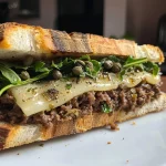['Close-up of a juicy ground beef and celery root sandwich on a brioche bun.', 'Side view of a delicious sandwich filled with ground beef and creamy celery root spread.', 'A mouthwatering sandwich showcasing ground beef and celery root, garnished with fresh greens.', 'Richly textured ground beef and celery root sandwich displayed on a rustic wooden surface.']