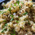 ['Close-up view of a bowl filled with herb and garlic quinoa mixed with colorful herbs.', 'Side angle shot of fluffy quinoa garnished with herbs and spices on a wooden table.', 'Textured close-up of cooked quinoa with visible garlic and herbs, served in a rustic dish.', 'Detailed image of herb and garlic quinoa, showcasing grains and seasoning blend.']
