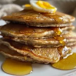 ['Close-up view of fluffy whole wheat honey pancakes stacked on a plate, glistening with honey.', 'Side view of warm, golden-brown pancakes drizzled with honey, topped with butter and cinnamon.', 'Mouthwatering whole wheat honey pancakes garnished with a pat of butter and honey drizzle.', 'Delicious stack of whole wheat honey pancakes served on a white plate with a rustic background.']
