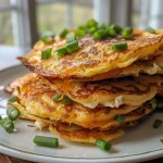 ['Close-up of golden-brown potato pancakes stacked on a plate, with visible green onion pieces.', 'Side view of crispy potato pancakes topped with shredded cheddar cheese, showcasing their texture.', 'Juicy high protein potato pancakes arranged on a wooden table, highlighting their savory ingredients.', 'Freshly cooked potato pancakes sizzling in oil, displaying a rich golden hue and garnished with green onions.']