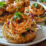 ['Close-up view of a sesame bagel topped with honey-lime shrimp and chili mayo.', 'Side view of a sesame bagel filled with shrimp, garnished with cilantro on a plate.', 'Juicy honey-lime shrimp on a toasted sesame bagel with a drizzle of chili mayo.', 'Slice of sesame bagel showcasing shrimp, lime, and a creamy red sauce on top.']