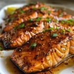 ['Close-up view of Spicy Honey Garlic Salmon garnished with sesame seeds and green onions.', 'Side view of juicy Spicy Honey Garlic Salmon on a plate with lemon wedges.', 'Colorful presentation of honey-glazed salmon drizzled with sauce and topped with herbs.', 'Detailed shot of salmon fillets glistening with spicy honey garlic sauce.']