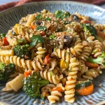 ['A close-up view of a colorful vegan pasta stir-fry featuring fusilli pasta and assorted vegetables.', 'A vibrant dish of vegan pasta stir-fry with broccoli, carrots, and mushrooms, garnished with cilantro.', 'A side view of a delicious vegan pasta stir-fry, showcasing colorful ingredients like zucchini and garlic.', 'A plate of juicy vegan pasta stir-fry with a variety of fresh vegetables in a savory sauce.']