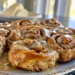 Close-up of freshly baked apple cinnamon rolls drizzled with cream cheese frosting.
