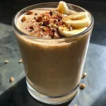 Close-up view of a creamy Chai Smoothie in a glass with a straw, garnished with spices.