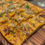 Close-up view of a slice of Garlic Pumpkin Flatbread, showcasing its golden-brown crust and topped with garlic pieces.