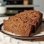 Side view of a moist gingerbread loaf with a golden-brown crust on a wooden board.