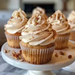 Close-up side view of moist maple cupcakes topped with maple cream cheese frosting and chopped pecans.