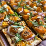 Close-up side view of a roasted butternut squash flatbread topped with arugula and feta cheese.