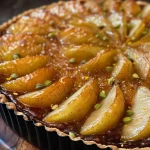 A close-up side view of a saffron poached pear tart with pistachios.