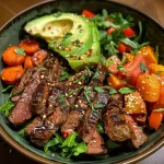 Close-up of a colorful Steak Power Bowl featuring sliced steak, roasted vegetables, avocado, and leafy greens.