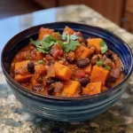 Close-up side view of a bowl of sweet potato chili garnished with lime wedges and fresh cilantro.